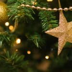 Close-up of a Christmas tree with golden star and ornament, shimmering lights and festive decorations.